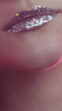 Vertical video. Glitter lips. Party makeup. Artistic visage. Cropped closeup of woman face with sparkling metallic silver gloss in red neon color light.