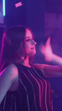 Mutlu kadınlar. Dans eden arkadaşlar. Gece partisi. Neşeli bayanlar konfeti yağmurunda dans ederken neon ışığı mor ışıkta. Dikey video.