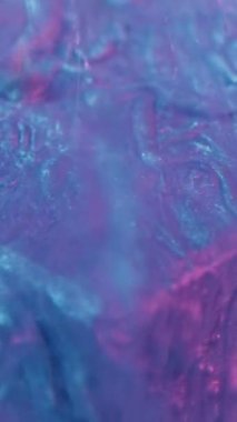 Vertical video. Neon fluid. Ink splash. Sparkling frost. Defocused blue pink color light glitter paint drop motion on cube edge in water abstract background.