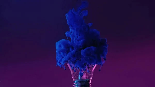 Ink shot in broken lamp. Neon background. Blue color fluid splash smoke cloud filling cracked glass light bulb in water on dark purple abstract copy space.