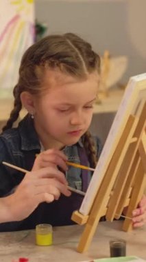 Vertical video. Art school. Kid talent. Creative leisure. Female teacher little girl painting together with paintbrushes on easel in studio.