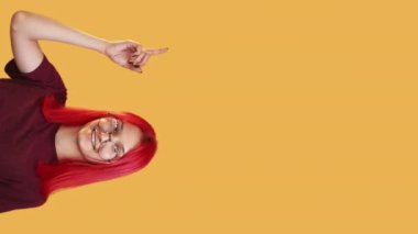 Vertical video. Recommending offer. Solution idea. Cheerful girl pointing up finger showing orange empty space background for text or product advertising content.