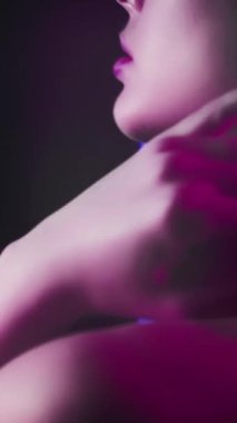 Vertical video. 90s fashion. Neon model. Retro 2000s look. Cropped profile portrait of teen girl face posing in purple pink color flash light on dark.
