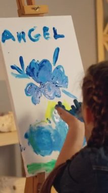 Vertical video. Kid creativity. Painting art. Young artist talent. Inspired small girl blowing off glitter from hands on blue yellow color angel artwork.