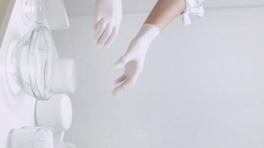 Vertical video. Cosmetology salon. Female worker. Product variety. Unrecognizable woman hands in gloves put in order cosmetic bottles at workplace.