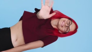 Vertical video. Hello greeting. Hey salute. Nice meeting. Happy cheerful girl peeking out waving hand hi on blue background seamless loop.