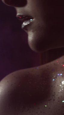 Vertical video. Glitter makeup. Glamour look. Disco beauty. Cropped closeup of woman face with shimmering shiny skin metallic lips in neon blue red color night light on dark.