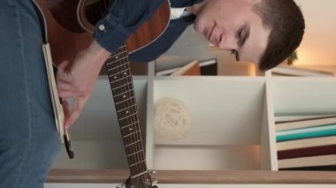 Vertical video. Song writing. Male composer. Home leisure. Creative man making notes in journal playing guitar sitting light room interior.