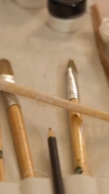 Vertical video. Art supplies. Painting workplace. Closeup of acrylic gouache paint bottles palette still life picture canvas paintbrush tools set organizer.