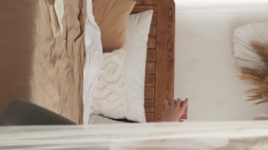 Vertical video. Weekend laziness. Relaxed woman. Enjoying rest. Beautiful calm lady with cup of coffee sitting bed for read book in light home interior.