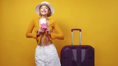 Vacation excitement. Happy woman. Inspiration mood. Pretty expressive lady in summer look holding foreign passport with tickets posing near suitcase on yellow background.