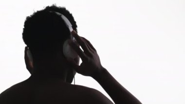 Music chill. Sound technology. Back view silhouette of unrecognizable relaxed man in headphones enjoying listening to audio dancing isolated on white free space background.