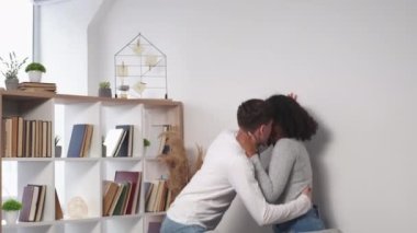 Passion love. Excited couple. Home intimacy. Happy beloved man and woman kissing and hiding under sofa embracing light room interior.