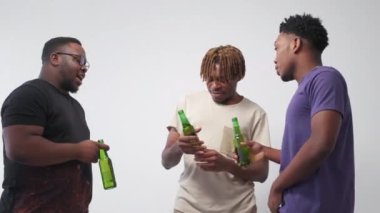 Friendly meeting. Positive black men. Enjoying communication. Relaxed hipster guys talking together with beer bottles posing on light background.