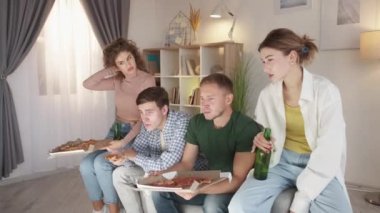 Horror movie. Shocked friends. Home leisure. Relaxed men and women feeling disgust watching thriller video sitting sofa with pizza and beer in light room interior.
