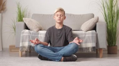 Home meditation. Peaceful boy. Tranquil energy. Calm casual teenager sitting floor in yoga pose moving in relaxing rhythm light room interior.