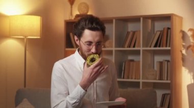 Unhealthy food. Addicted man. Diet problem. Pleased inspired guy holding smelling plate with sweet doughnut but female hand proposing apple light shadow room interior.