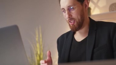 Online conference. Business man. Digital connection. Positive smart man talking to laptop explaining information in light room interior.
