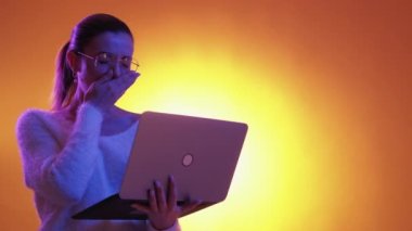 Boring work. Tired woman. Neon light portrait. Exhausted lady holding laptop yawning falling asleep on purple orange background copy space.