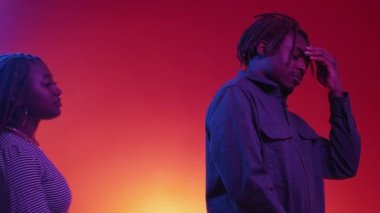 Close relationship. Beloved couple. Neon light portrait. Careful black woman embracing depressed man to calm down on red blue background.