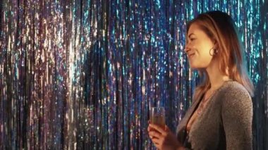 Christmas party. Festive woman. Holiday celebration. Elegant happy lady with glass champagne posing on light blue silver cascade curtain background copy space.