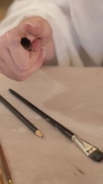 Vertical video. Painting tools. Art supplies. Creative workplace. Closeup of professional female artist hand choosing paintbrush from set on table.