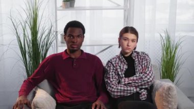Problem relationship. Offended couple. Diverse people. Unhappy european woman and black man sitting together on sofa in light room interior.