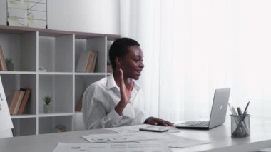 Virtual conference. Video chat. Business telecommuting. Satisfied cheerful female leader waving hello on notebook discussing project at light home office interior with free space.