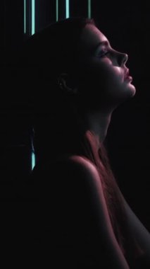 Vertical video. 90s fashion. Night model. Retro look. Profile silhouette of confident teen girl face posing in blue color neon light on dark black.