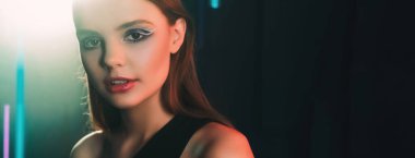 90s model. Retro fashion. Old 2000s look. Portrait of confident teen girl face with artistic makeup in purple blue color neon light on dark black empty space background.