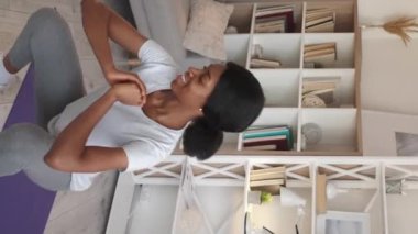 Vertical video. Squat exercise. Sporty woman. Home aerobics. Happy motivated sportswoman doing fitness training for legs buttocks light room interior.