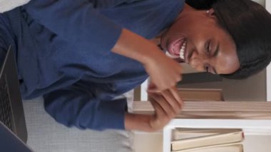 Vertical video. Online win. Internet lottery. Female success. Excited woman raising hands up celebrating great news taking laptop in light home interior.