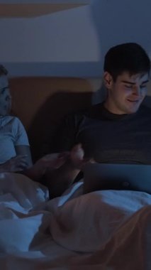 Çiftler kavga eder. Gece çatışması. İlişki sorunu. Üzgün, tatminsiz bir kadın, dikkatsiz kocaya bağırıyor. Geç saatte laptopla yatakta. Dikey video.