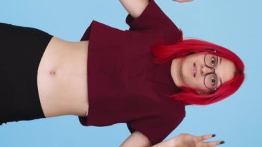 Vertical video. Clueless shrug. Careless whatever. Disappointed shocked confused girl peeking out raising shoulders on blue background seamless loop.