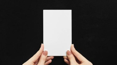 White note. Presentation card. Empty message. Female hands holding clean mockup paper sheet with copy space on black background.