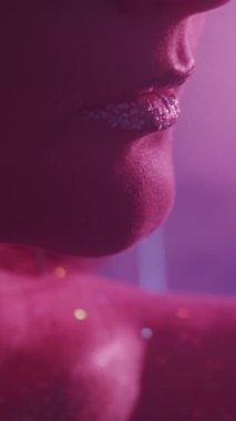 Vertical video. Neon beauty. Glitter makeup. Glamour art. Cropped closeup of pink color light woman face with sparkling skin metallic silver lips.