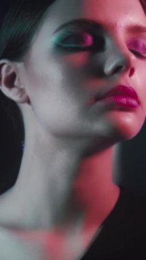 Vertical video. Disco fashion. 90s look. Retro 2000s beauty. Relaxed teen girl face with artistic makeup closed eyes dancing in red purple blue color neon flash light on dark.