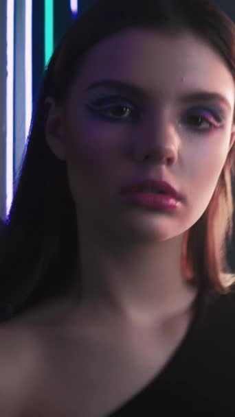 垂直录像 90年代的型号 复古时尚 老旧的2000年代 浅蓝色霓虹灯在深黑色背景下装扮的自信少女的画像 — 图库视频影像