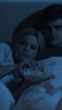 Korku filmi. Birkaç gece boş vakit. Geç saatte ev eğlencesi. Korkak kadın TV 'de korku filmi seyrediyor. Cesur koca, karanlık bir yatak odasında, parlak mavi ışıkla. Dikey video.