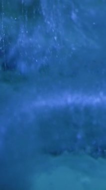 Vertical video. Glitter splash. Ink water. Ice flakes. Defocused blue color paint drop mist flow motion on frost ice texture surface abstract background.