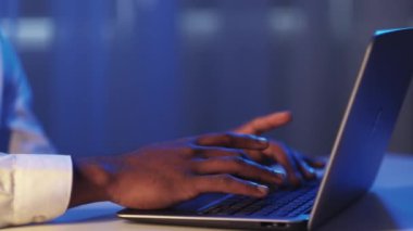 Late work. Software engineering. Information technology. Male developer hands typing using notebook at dark night blue neon light digital office.