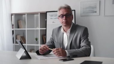 Business coaching. Successful career. Online interview. Confident smart cheerful senior entrepreneur man speaking at light modern office workplace interior.