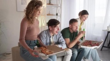 Watching TV. Happy friends. Home leisure. Excited laughing men and women eating pizza drinking beer with funny movie in light room interior.