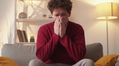 Money lost. Desperate man. Extra charge payments. Sad guy crying cleaning tears blowing nose with false cash dollars sitting sofa in light room interior.