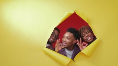 Ok sign. Satisfied black men. Great place. Happy male friends looking from yellow disrupted paper showing approved gesture on red background copy space.