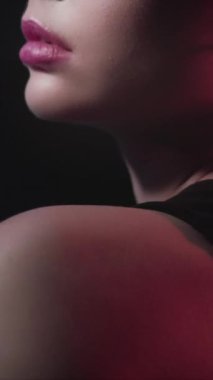 Vertical video. Fashion beauty. 90s look. Retro vogue. Cropped profile portrait of woman model face posing in red purple color neon flash light on dark.