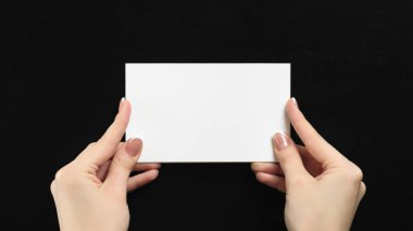 Mockup letter. Advertising card. Information note. Female hands holding blank white paper sheet with empty space on black background.