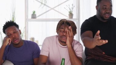 Sport fail. Depressed male friends. Home meeting. Unhappy black men feeling disappointed looking translation on TV with beer bottles in light room interior.