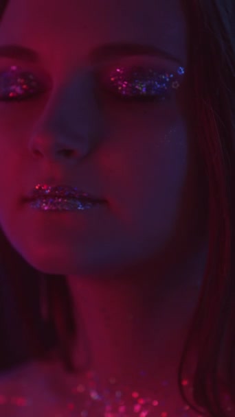 垂直ビデオ ネオンの顔 キラキラしたメイク ディスコファッション 赤い色の光輝く肌を持つリラックスした女性金属アイシャドウ唇楽しいですダンスオンダーク — ストック動画