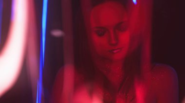 Neon face. Disco beauty. Party look. Defocused red blue color light flare woman with sparkling face skin glitter makeup on dark free space.